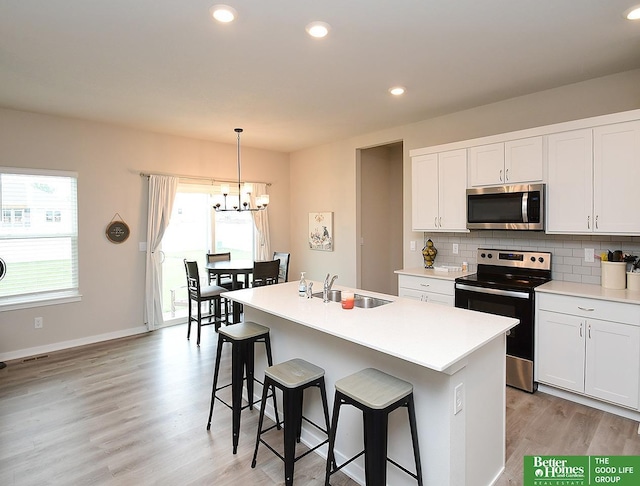 kitchen with stainless steel appliances, a sink, a chandelier, light wood-style flooring, and backsplash