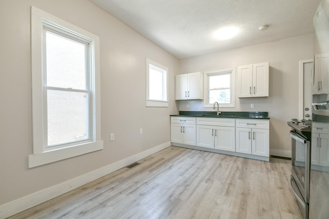 3021 N St, Lincoln, NE 68510 - kitchen with light wood-type flooring, a sink, white cabinetry, baseboards, and dark countertops