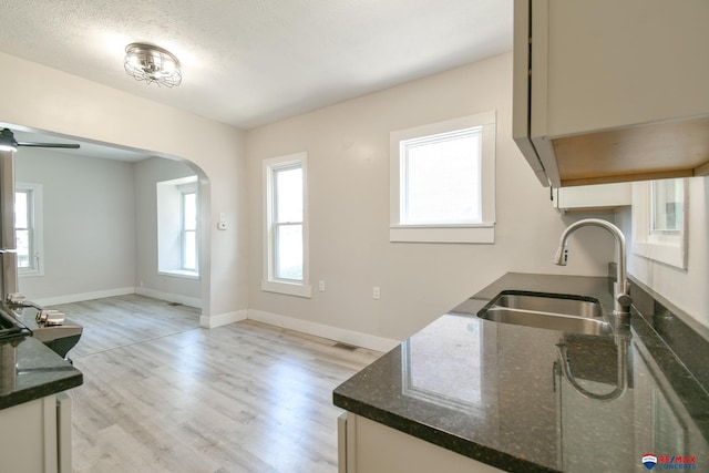 3021 N St, Lincoln, NE 68510 - kitchen featuring a sink, arched walkways, light wood finished floors, and dark stone countertops