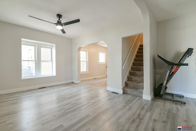 3021 N St, Lincoln, NE 68510 - unfurnished living room featuring arched walkways, a ceiling fan, light wood-style flooring, stairs, and baseboards
