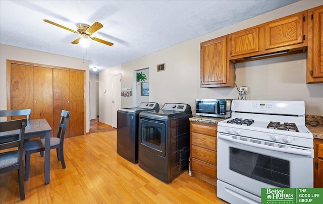 6070 Buckingham Ave, Omaha, NE 68117 - kitchen with white range with gas stovetop, light wood-style flooring, stainless steel microwave, brown cabinets, and washing machine and dryer
