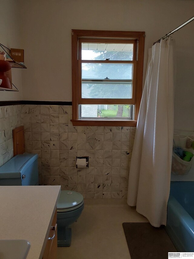7027 S 39th Ave, Bellevue, NE 68147 - bathroom with tile walls, toilet, vanity, a wainscoted wall, and shower / bath combo