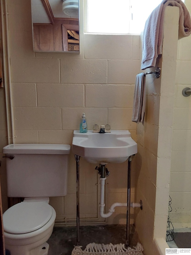 7027 S 39th Ave, Bellevue, NE 68147 - bathroom featuring concrete block wall, toilet, unfinished concrete flooring, and a sink