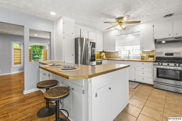 8207 Decatur St, Omaha, NE 68114 - kitchen featuring stainless steel appliances, under cabinet range hood, a sink, white cabinetry, and a textured ceiling