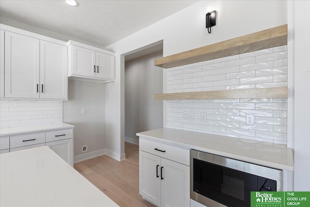 5729 N 196th St, Elkhorn, NE 68022 - kitchen with stainless steel microwave, backsplash, light wood-style flooring, white cabinetry, and baseboards