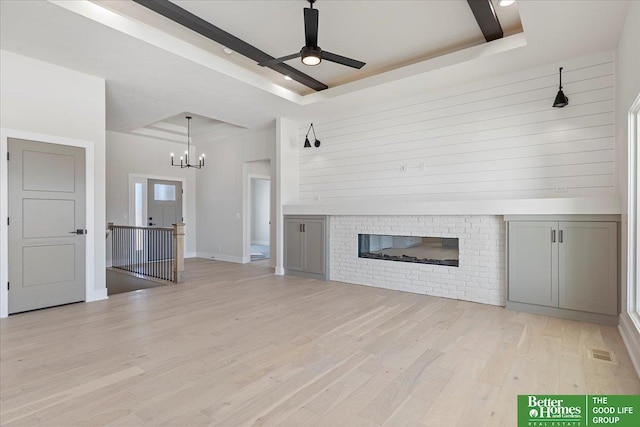 5729 N 196th St, Elkhorn, NE 68022 - unfurnished living room with a raised ceiling, light wood-type flooring, a brick fireplace, a ceiling fan, and a chandelier