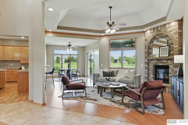 211 Longwood Dr, Papillion, NE 68133 - living area featuring a ceiling fan, a tray ceiling, a fireplace, light wood-style flooring, and baseboards