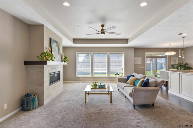 15301 Kansas Ave, Omaha, NE 68116 - carpeted living area featuring a ceiling fan, a tile fireplace, recessed lighting, baseboards, and a tray ceiling