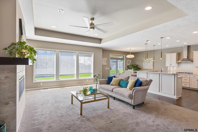 15301 Kansas Ave, Omaha, NE 68116 - living room featuring ceiling fan, a tray ceiling, recessed lighting, a glass covered fireplace, and dark wood-style flooring