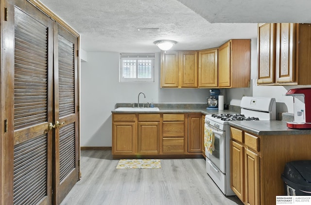 6920 N 30th St, Omaha, NE 68112 - kitchen with white gas stove, a sink, light wood-style flooring, brown cabinetry, and a textured ceiling
