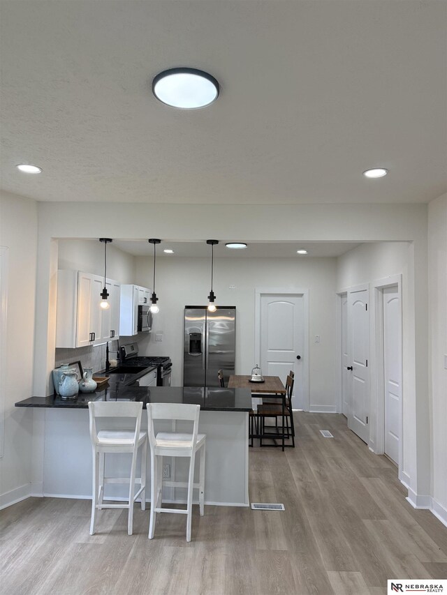 914 S 26th St, Omaha, NE 68105 - kitchen with appliances with stainless steel finishes, dark countertops, light wood-style flooring, white cabinetry, and a peninsula