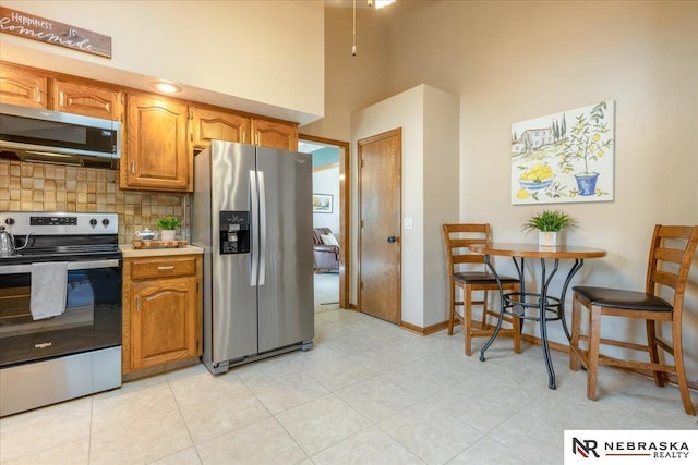 926 Iron Rd, Papillion, NE 68046 - kitchen with appliances with stainless steel finishes, a towering ceiling, tasteful backsplash, brown cabinets, and light countertops