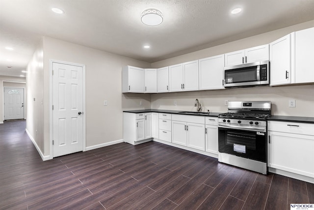 5437 S 18th St, Omaha, NE 68107 - kitchen featuring stainless steel appliances, a sink, dark wood finished floors, dark countertops, and white cabinetry