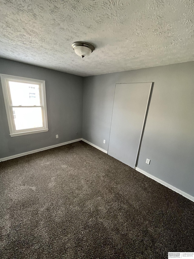 1152 N D St, Fremont, NE 68025 - unfurnished bedroom featuring baseboards, dark carpet, and a textured ceiling