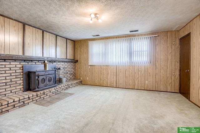 3209 Coffey Ave, Omaha, NE 68123 - unfurnished living room with wooden walls, a textured ceiling, carpet, a wood stove, and baseboards