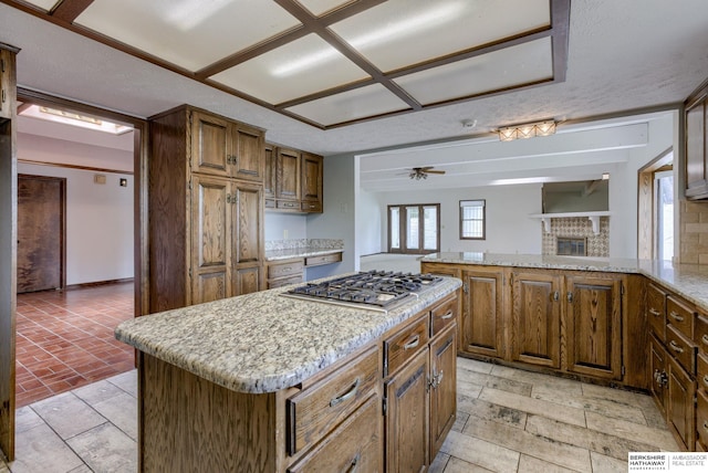 1905 S 116th St, Omaha, NE 68144 - kitchen featuring stainless steel gas cooktop, ceiling fan, a kitchen island, a glass covered fireplace, and light stone counters