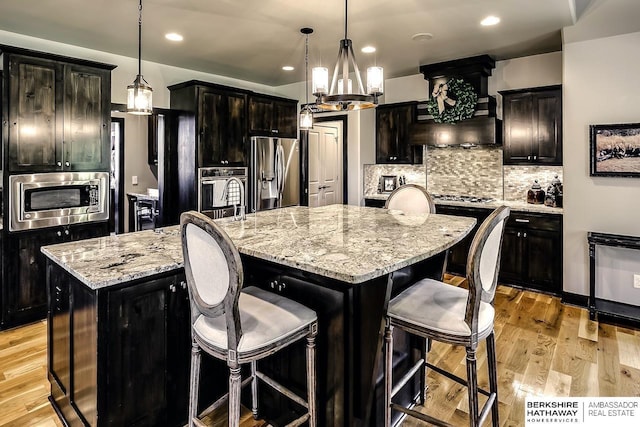 3334 S 188th Ave, Omaha, NE 68130 - kitchen featuring appliances with stainless steel finishes, a large island with sink, custom range hood, a breakfast bar area, and backsplash
