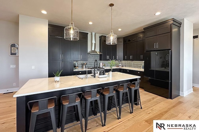 11473 S 189th St, Gretna, NE 68028 - kitchen featuring wall chimney range hood, freestanding refrigerator, a breakfast bar, backsplash, and light wood finished floors