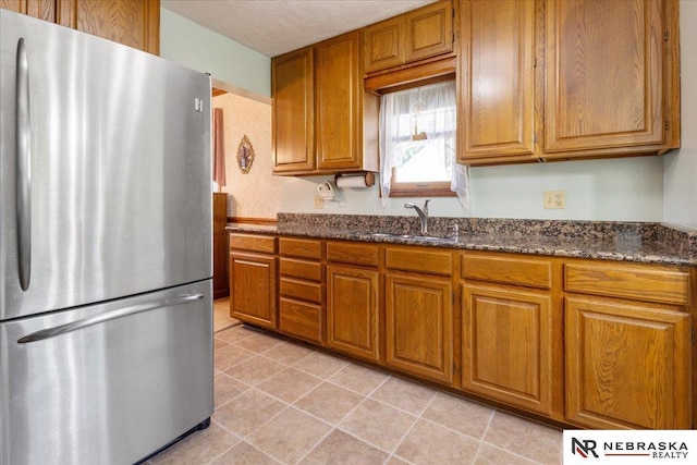 4542 Charles St, Omaha, NE 68132 - kitchen with freestanding refrigerator, brown cabinetry, a sink, dark stone counters, and light tile patterned flooring