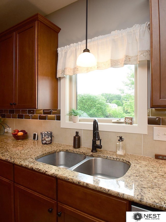 7521 Exbury Rd, Lincoln, NE 68516 - kitchen with a sink, tasteful backsplash, brown cabinetry, light stone countertops, and pendant lighting