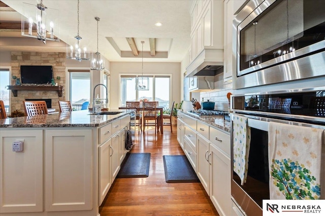 12601 S 78th St, Papillion, NE 68046 - kitchen featuring appliances with stainless steel finishes, a sink, a tray ceiling, light wood-style flooring, and stone countertops