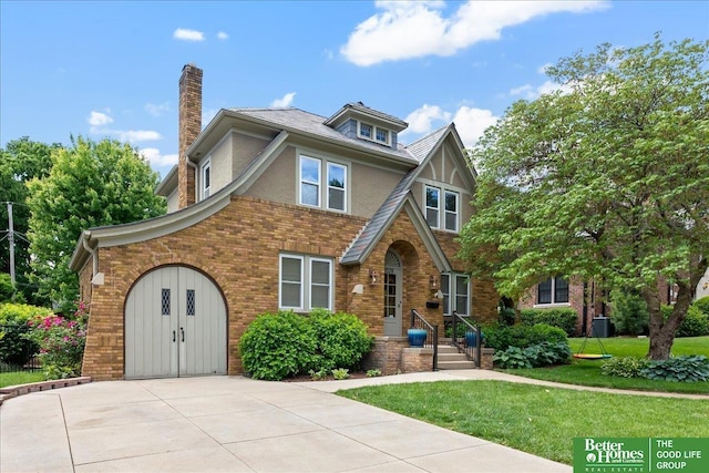 2028 N 55th St, Omaha, NE 68104 - tudor house with a front yard, concrete driveway, a chimney, brick siding, and stucco siding