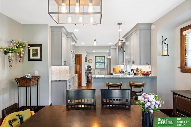 2028 N 55th St, Omaha, NE 68104 - kitchen featuring gray cabinets, built in microwave, stainless steel fridge, light stone countertops, and backsplash