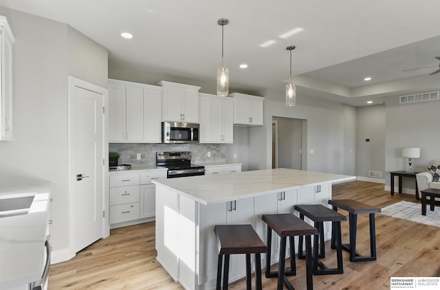 6320 Harvest Dr, Papillion, NE 68133 - kitchen featuring appliances with stainless steel finishes, tasteful backsplash, light wood-style flooring, white cabinets, and a kitchen breakfast bar
