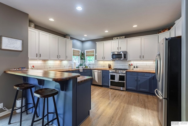 15210 Craig Cir, Bennington, NE 68007 - kitchen with appliances with stainless steel finishes, blue cabinetry, butcher block counters, a peninsula, and white cabinets