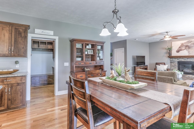 10311 S 124th St, Papillion, NE 68046 - dining room featuring light wood-type flooring, ceiling fan, a stone fireplace, a chandelier, and baseboards