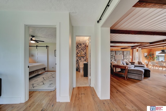 209 N Maloney Dr, North Platte, NE 69101 - corridor with light wood finished floors, a barn door, beam ceiling, a textured ceiling, and baseboards