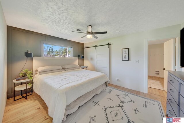 209 N Maloney Dr, North Platte, NE 69101 - bedroom with light wood-style flooring, a textured ceiling, a barn door, and ceiling fan