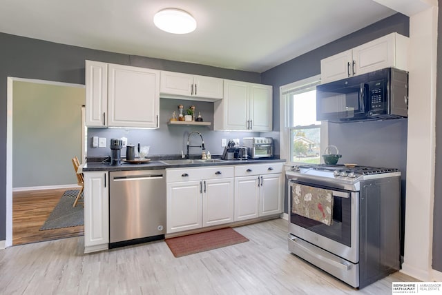 4332 Vinton St, Omaha, NE 68105 - kitchen featuring stainless steel appliances, a sink, dark countertops, light wood-style flooring, and white cabinets