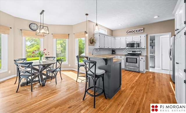 5517 S 174th Ave, Omaha, NE 68135 - kitchen featuring stainless steel appliances, a peninsula, a breakfast bar, backsplash, and light wood-type flooring