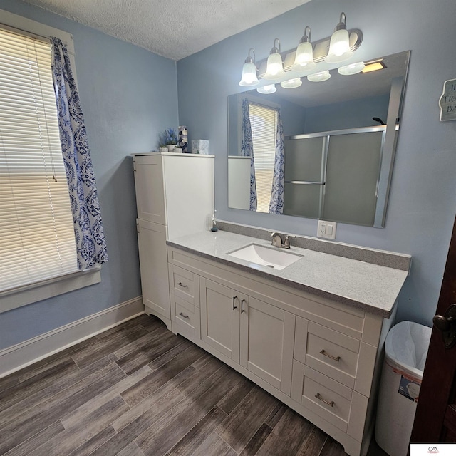 1119 H St, Fairbury, NE 68352 - bathroom with wood finished floors, an enclosed shower, vanity, a textured ceiling, and baseboards