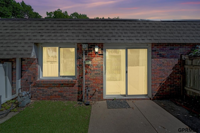 1625 Granada Ln, Lincoln, NE 68528 - exterior entry at dusk with roof with shingles, brick siding, and a yard