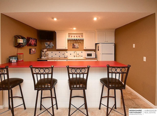5103 N 140th St, Omaha, NE 68164 - kitchen featuring white appliances, a sink, white cabinets, a kitchen breakfast bar, and recessed lighting