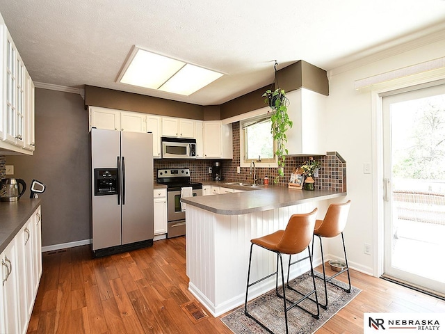 4219 Browning St, Lincoln, NE 68516 - kitchen featuring appliances with stainless steel finishes, decorative backsplash, hardwood / wood-style floors, a peninsula, and ornamental molding