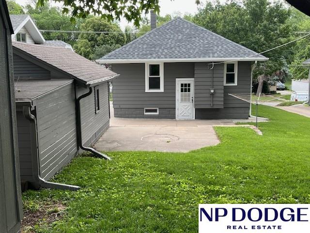 1406 S 55th St, Omaha, NE 68106 - rear view of property featuring roof with shingles, a yard, a chimney, and a patio
