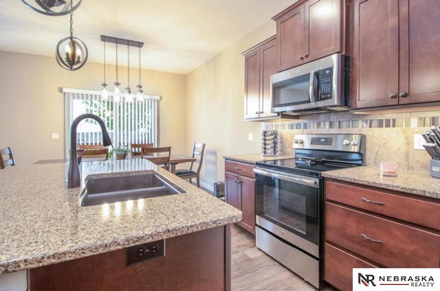 10425 S 110th St, Papillion, NE 68046 - kitchen featuring stainless steel appliances, a sink, decorative backsplash, hanging light fixtures, and light wood-style flooring