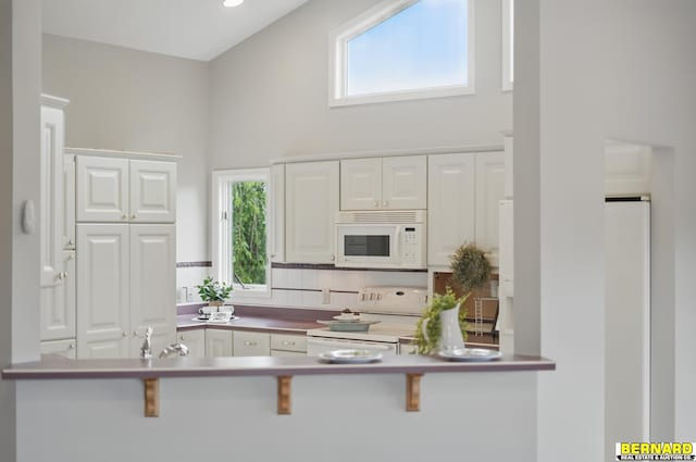 5665 I Rd, Nebraska City, NE 68410 - kitchen with white appliances, white cabinetry, healthy amount of natural light, a kitchen bar, and a high ceiling