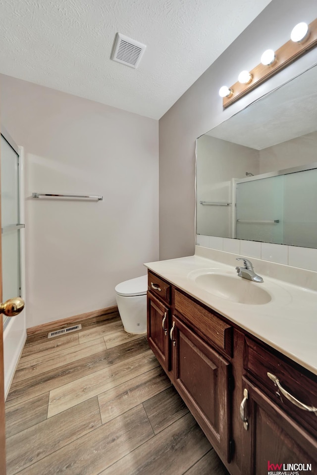 235 W Belmont Ave, Lincoln, NE 68521 - bathroom with vanity, a shower with shower door, wood finished floors, toilet, and a textured ceiling