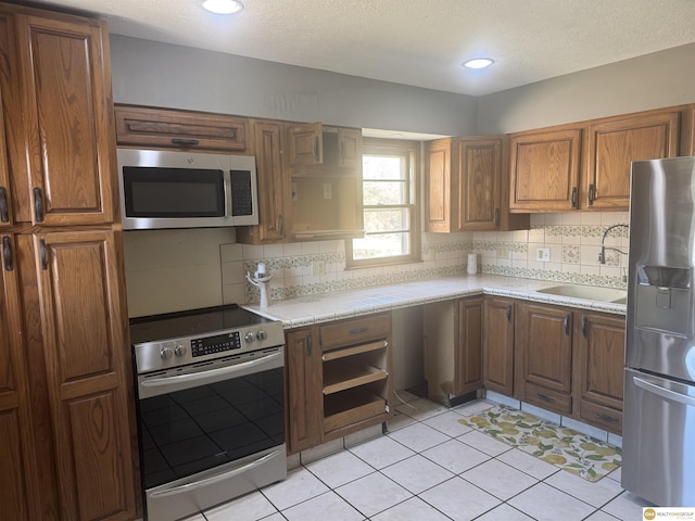7624 Nebraska Ave, Omaha, NE 68134 - kitchen with stainless steel appliances, a sink, decorative backsplash, brown cabinetry, and a textured ceiling