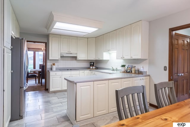 12212 Leavenworth Rd, Omaha, NE 68154 - kitchen with under cabinet range hood, freestanding refrigerator, black electric stovetop, a peninsula, and a sink