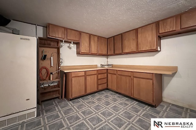 2203 Beaver Lake Blvd, Plattsmouth, NE 68048 - kitchen featuring freestanding refrigerator, dark flooring, brown cabinets, light countertops, and a textured ceiling