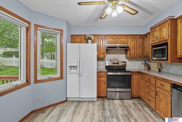 7432 Grand Oaks Dr, Lincoln, NE 68516 - kitchen featuring appliances with stainless steel finishes, under cabinet range hood, brown cabinetry, light wood-style floors, and tasteful backsplash