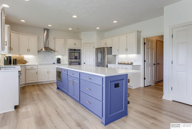 9711 S 176th St, Omaha, NE 68136 - kitchen featuring wall chimney range hood, stainless steel appliances, blue cabinetry, a kitchen island, and white cabinets