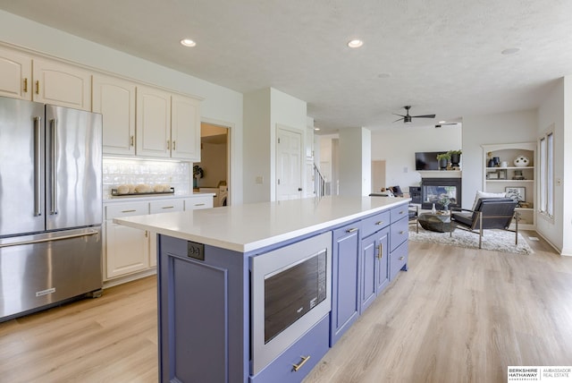 9711 S 176th St, Omaha, NE 68136 - kitchen featuring stainless steel appliances, light wood-style flooring, ceiling fan, a glass covered fireplace, and blue cabinetry