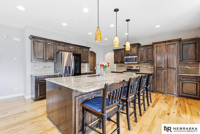 18402 Polk St, Omaha, NE 68135 - kitchen featuring stainless steel appliances, arched walkways, light wood-type flooring, recessed lighting, and a kitchen bar