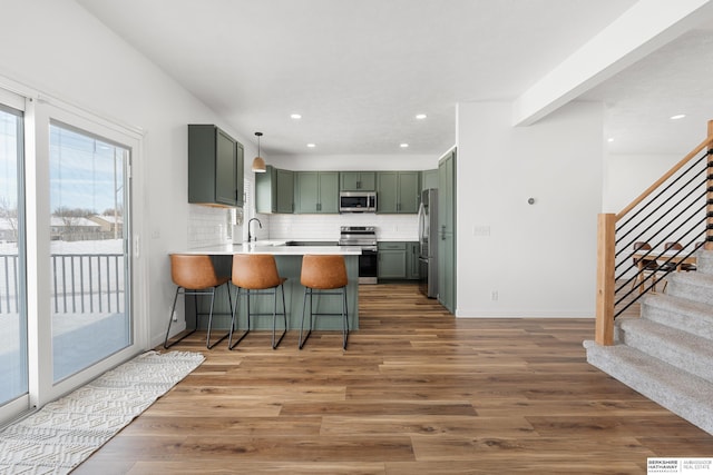 4706 S 187th Ave, Omaha, NE 68135 - kitchen with stainless steel appliances, green cabinetry, a peninsula, a kitchen bar, and wood finished floors